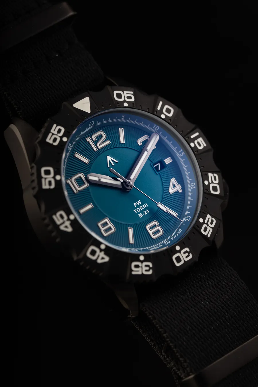 Pook Torni M-24 with teal-blue dial, date at 3 and black PVD case with 60-minute bezel on a black nylon strap